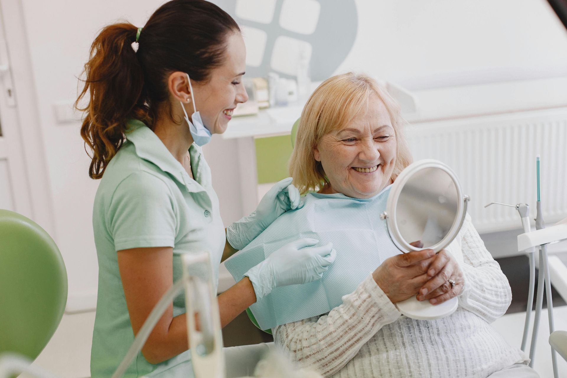 An elderly woman is looking at her teeth in a mirror at the dentist.