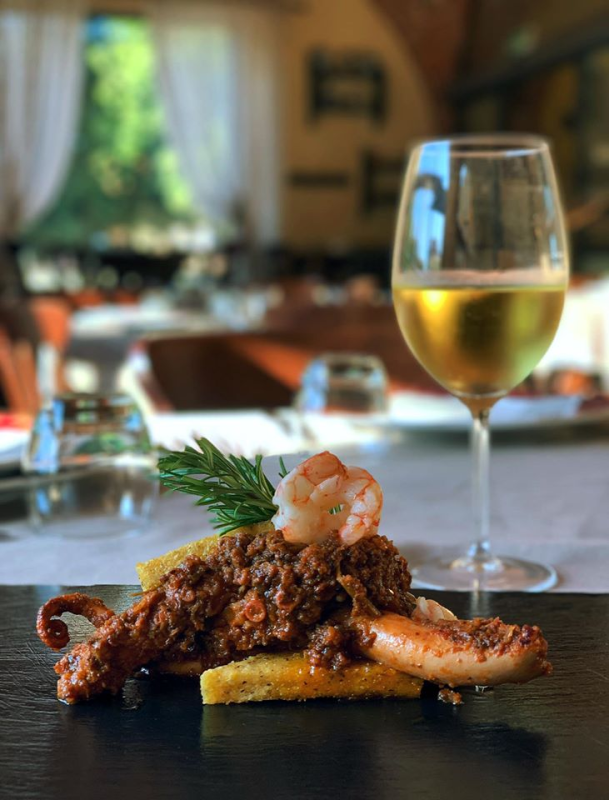 Piatto di polpo con gamberi, polenta, rosmarino e un bicchiere di vino bianco in un ristorante.