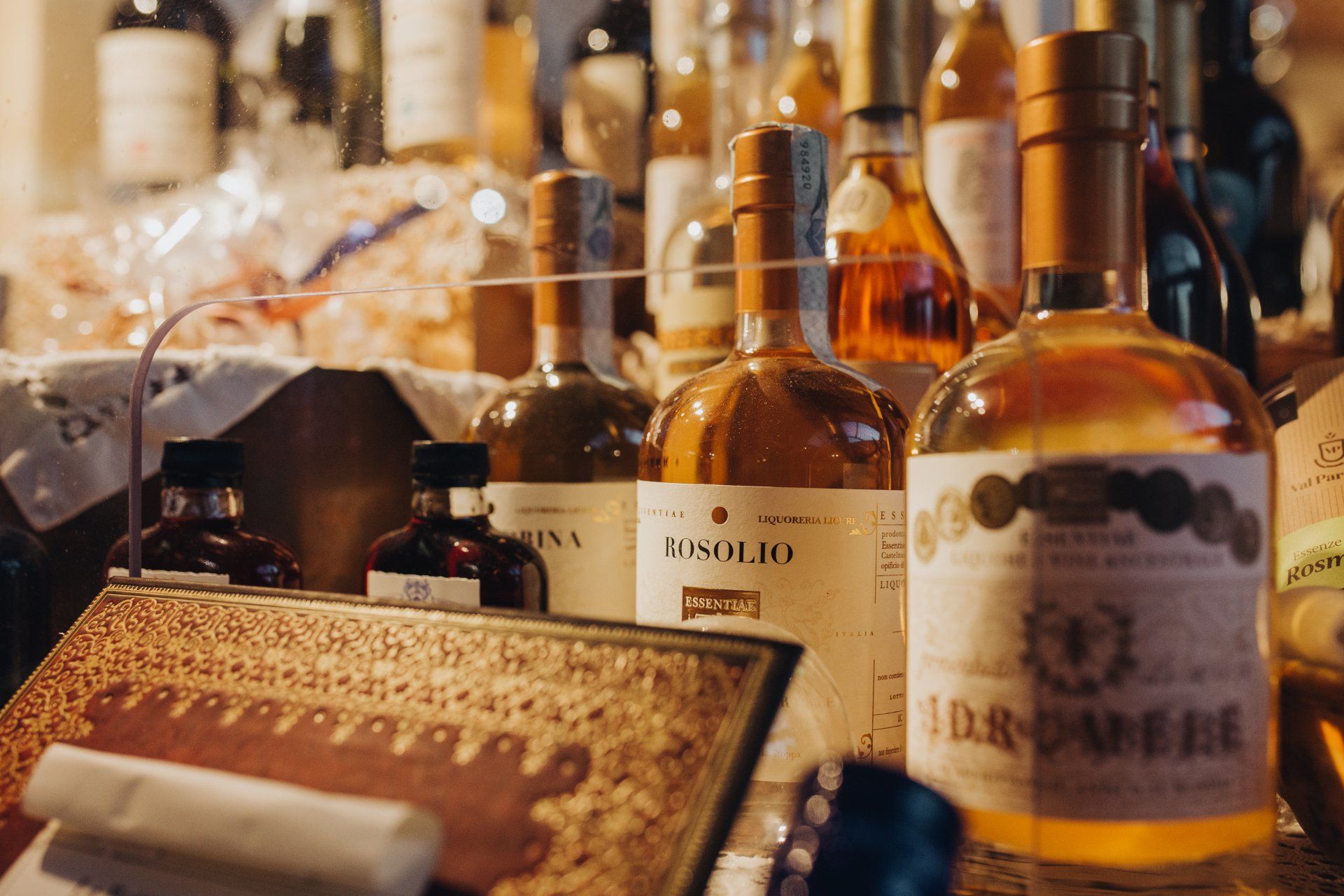 Bottiglie di liquore su uno scaffale, alcune con le etichette in vista. Illuminazione calda, colori intensi, forse un espositore da negozio.