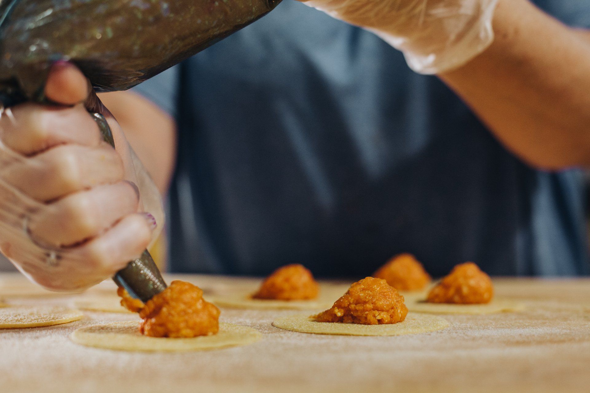 Una mano guantata versa il ripieno sulla pasta, preparando i ravioli.