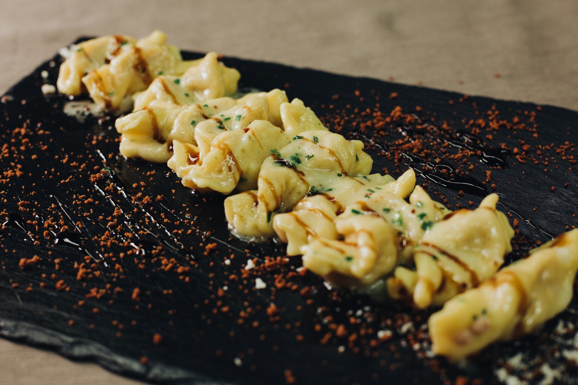 Piatto di pasta servito su una lavagna scura, condito con salsa e guarnito con polvere marrone.