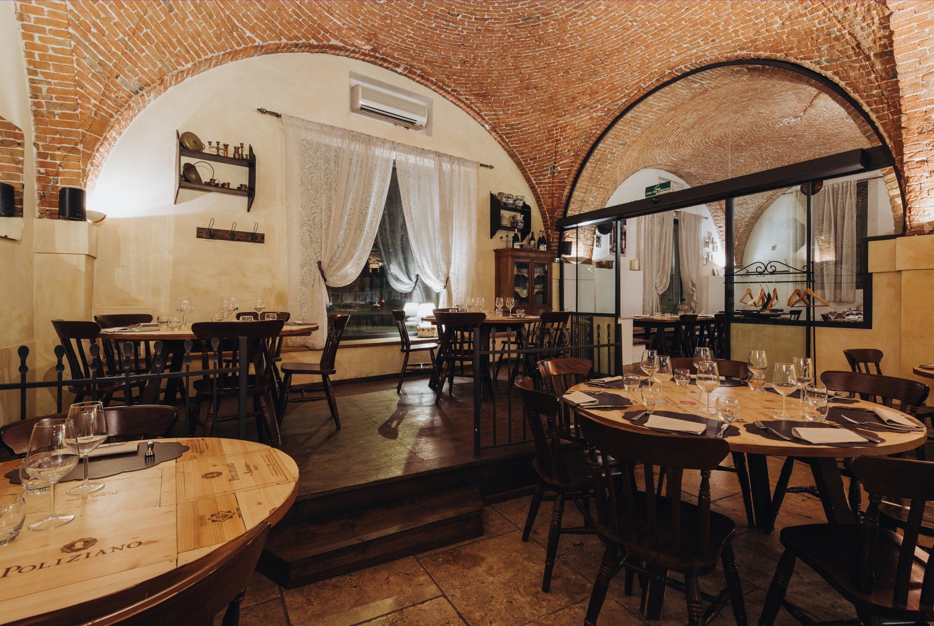Interno del ristorante con soffitto ad arco in mattoni, tavoli e sedie in legno. Illuminazione soffusa.