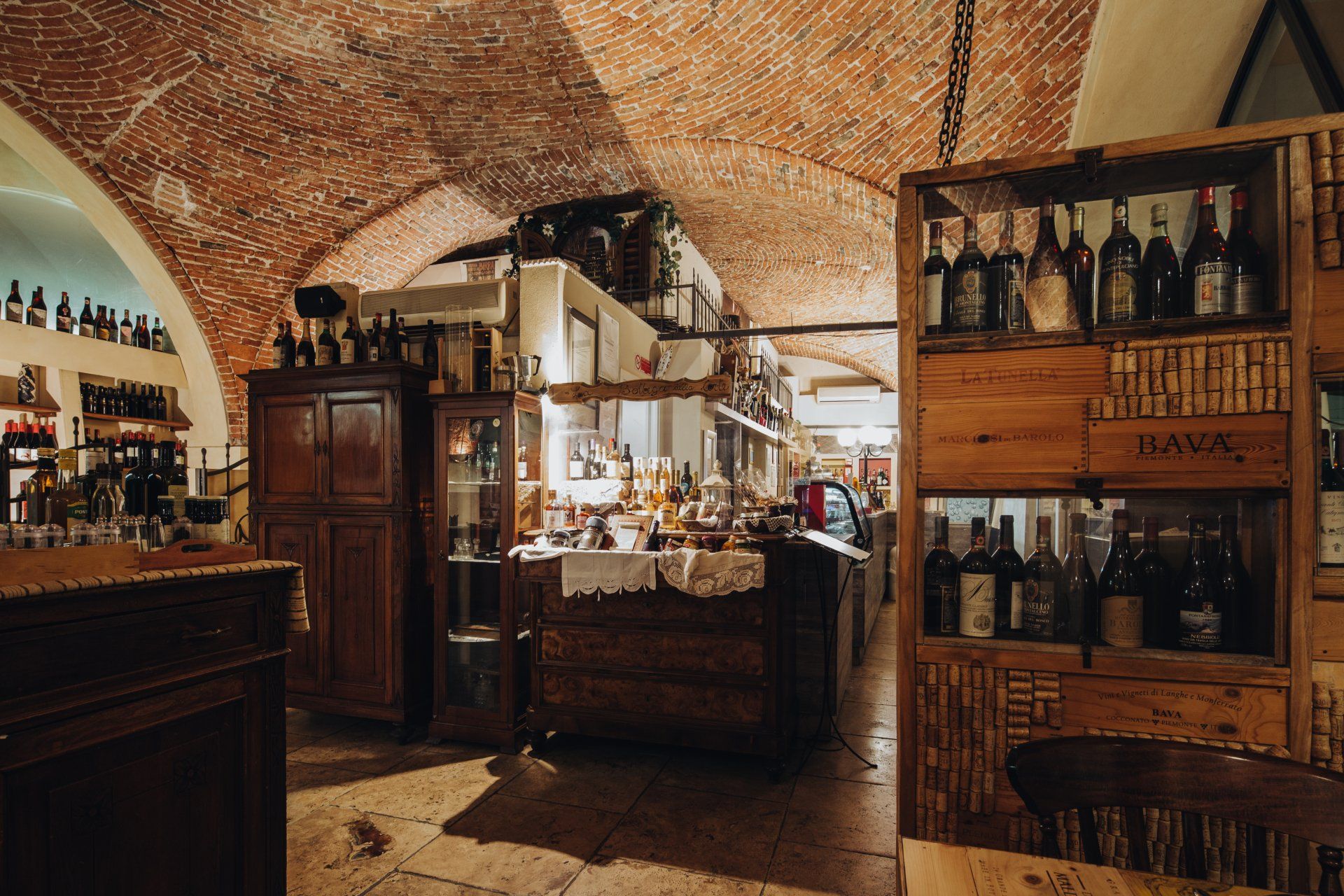 Accogliente cantina con soffitto in mattoni, scaffali in legno e bottiglie. L'illuminazione calda crea un'atmosfera rustica e invitante.