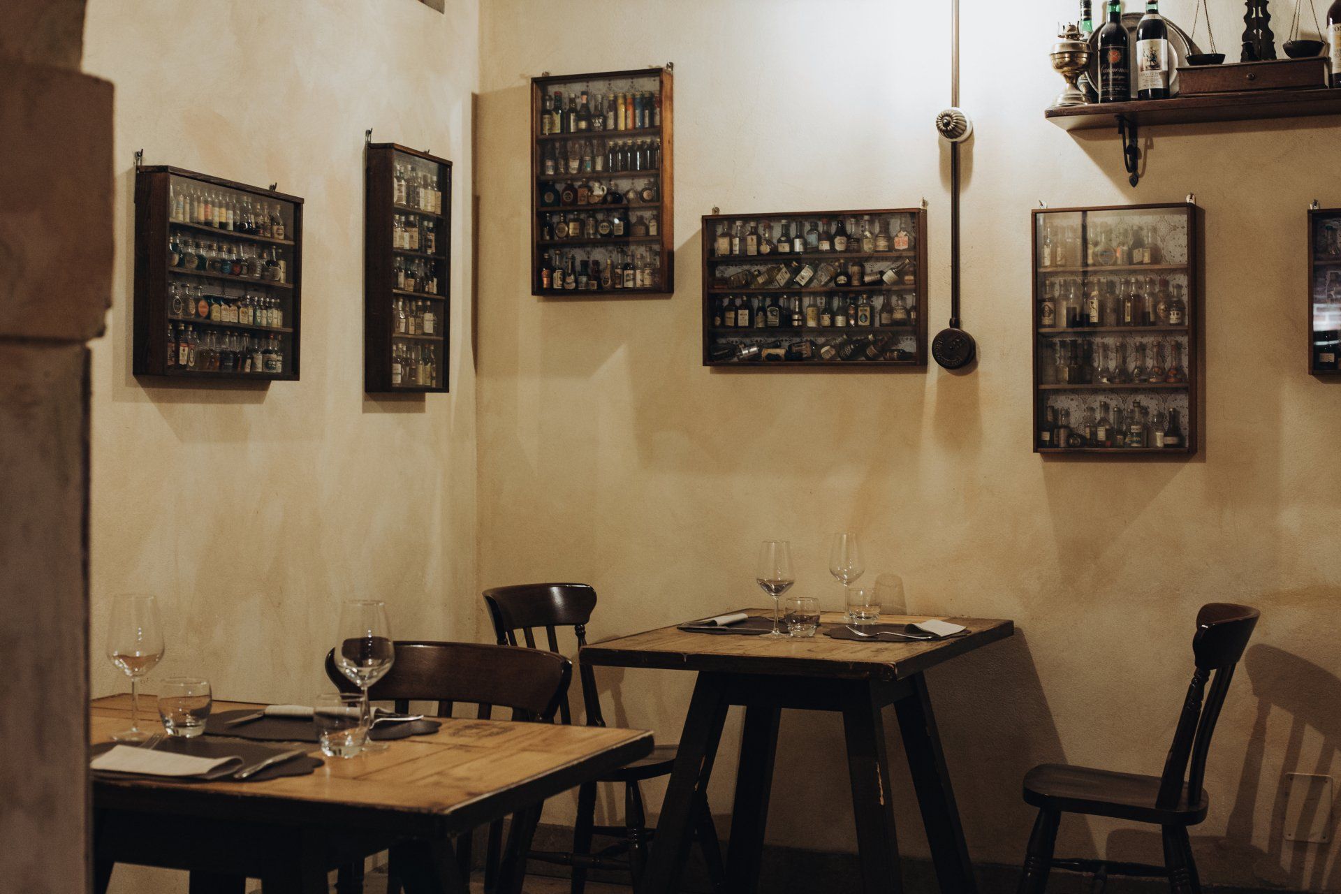 Accogliente ristorante con tavolini, sedie in legno ed esposizioni di bottiglie alle pareti.