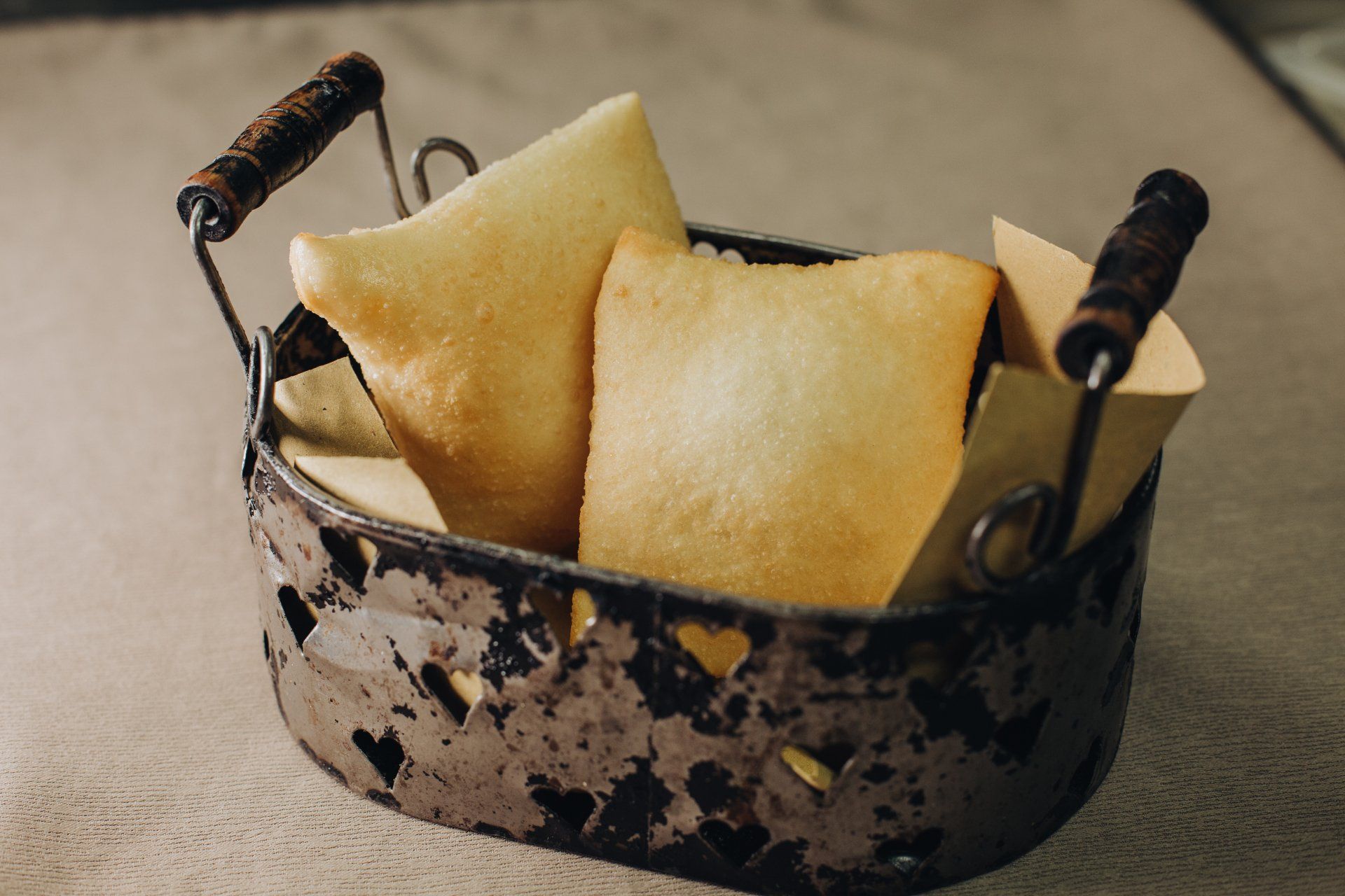 Due pasticcini dorati fritti in un cestino di metallo arrugginito con coni di carta.