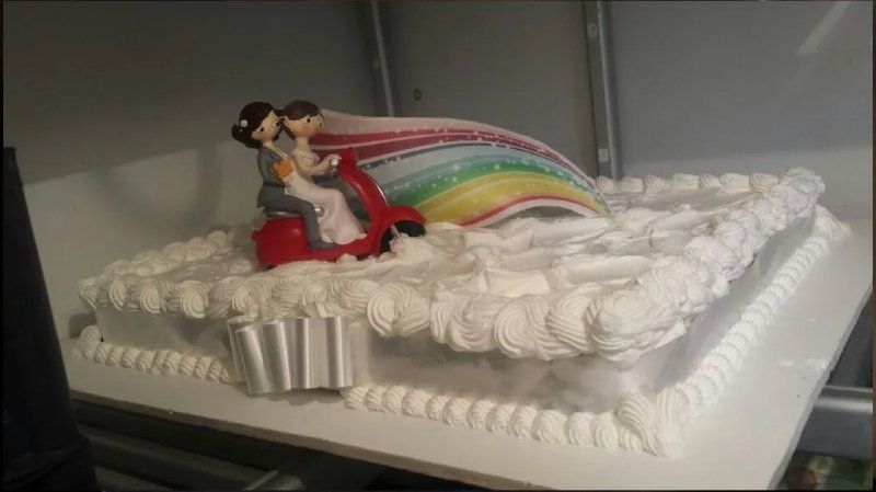 Torta nuziale con coppia in scooter, arcobaleno e glassa bianca.