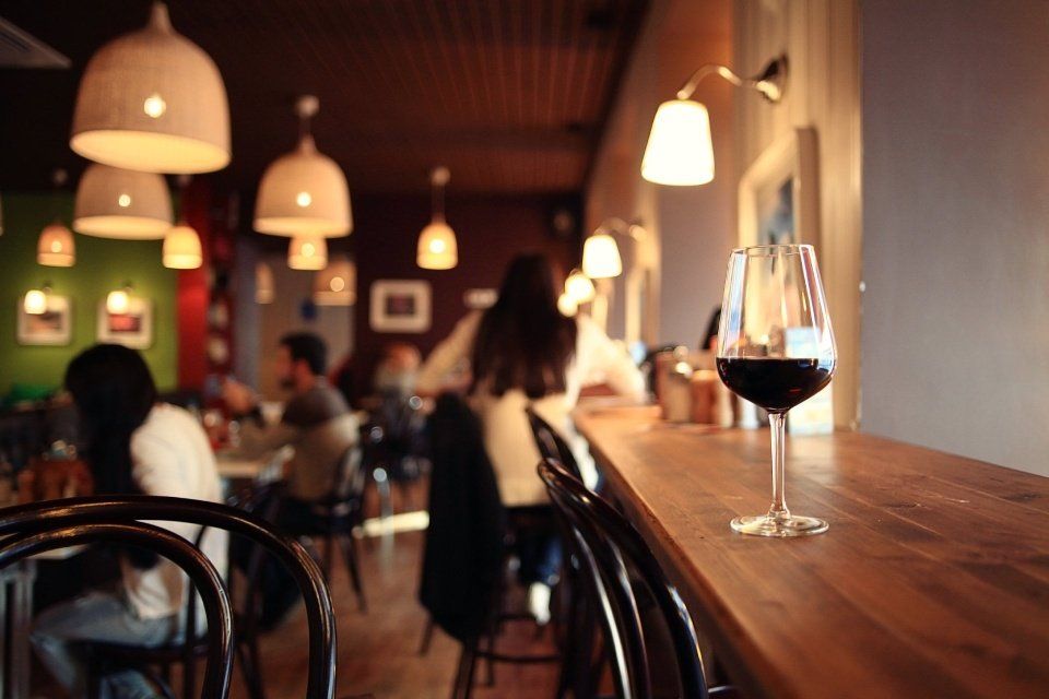 Un bicchiere di vino rosso su un bancone di legno in un ristorante illuminato in modo caldo, con clienti.