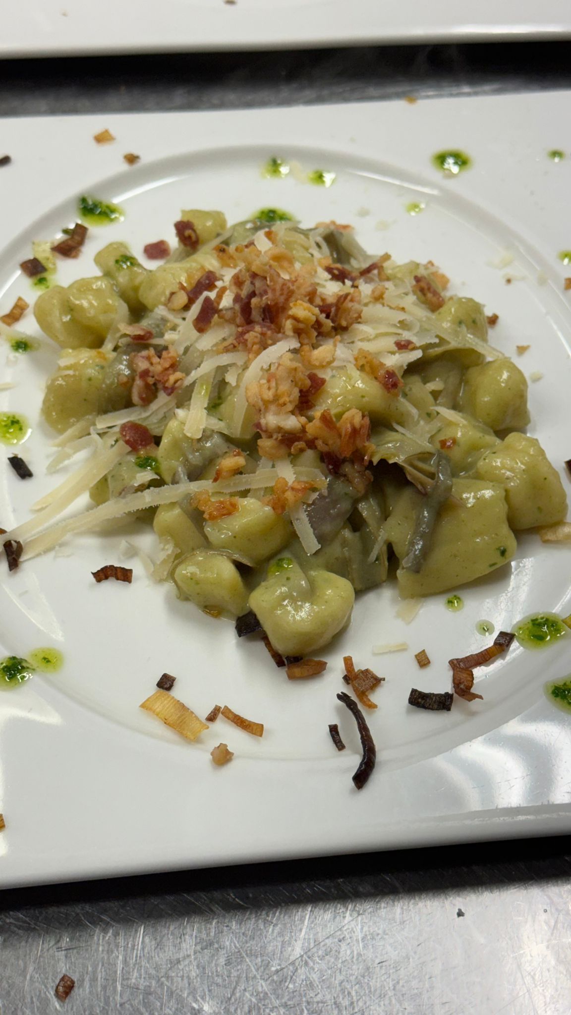 Piatto di gnocchi con sugo, formaggio grattugiato e pezzetti di pancetta, guarnito con olio verde.