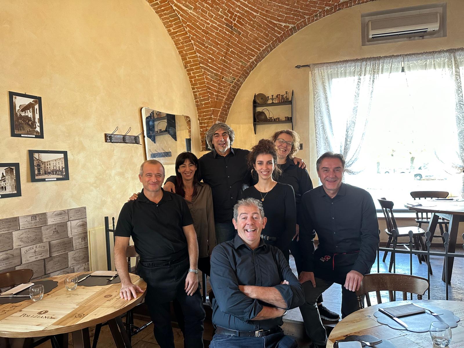 Il personale del ristorante posa davanti a un soffitto in mattoni. Pareti beige e tavoli in legno. Alcuni sorridono.