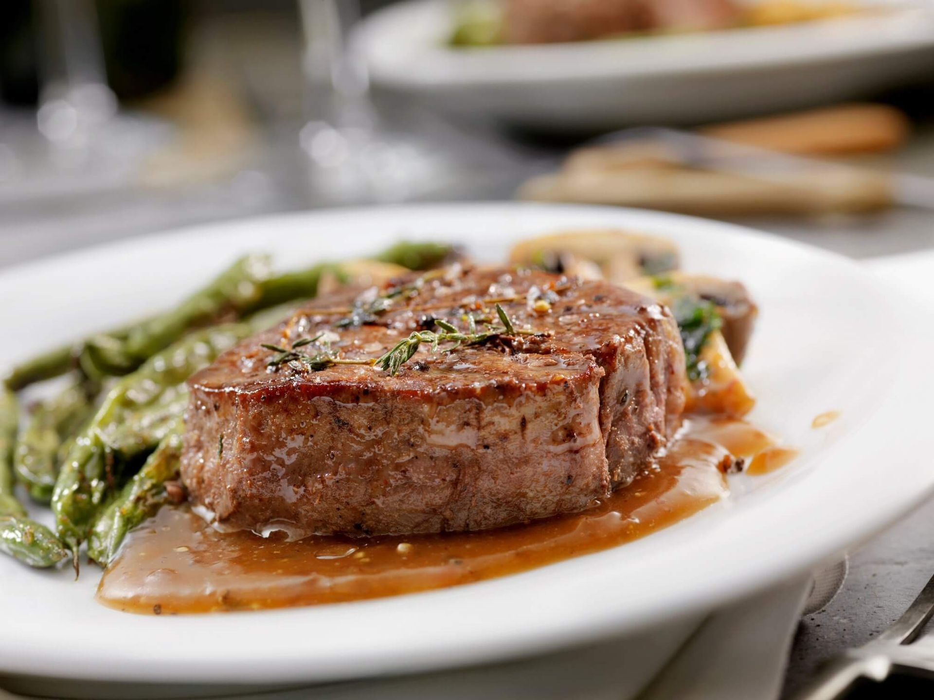 Bistecca con fagiolini e funghi, servita con salsa su un piatto bianco.