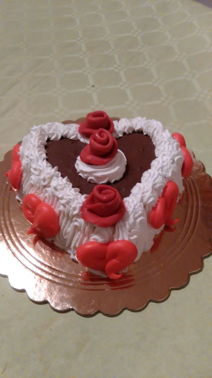 Torta a forma di cuore con glassa bianca, ripieno di cioccolato e decorazioni di rose rosse su un centrino dorato.