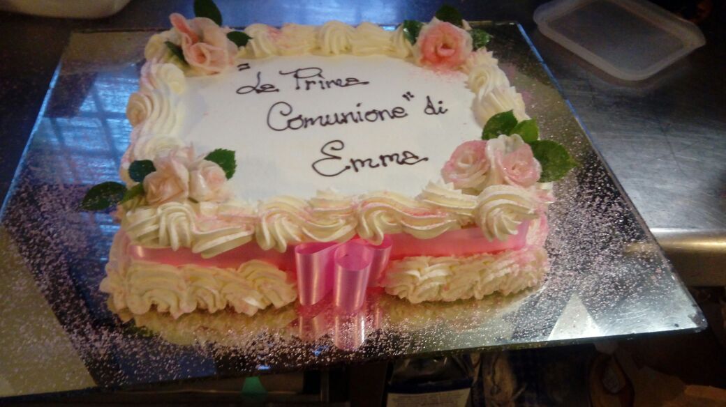 Una torta quadrata decorata con glassa rosa, fiori e la scritta