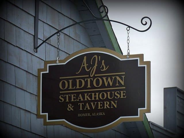 Sign for AJ's Oldtown Steakhouse & Tavern in Homer, Alaska. Brown and gold, hanging from a bracket.