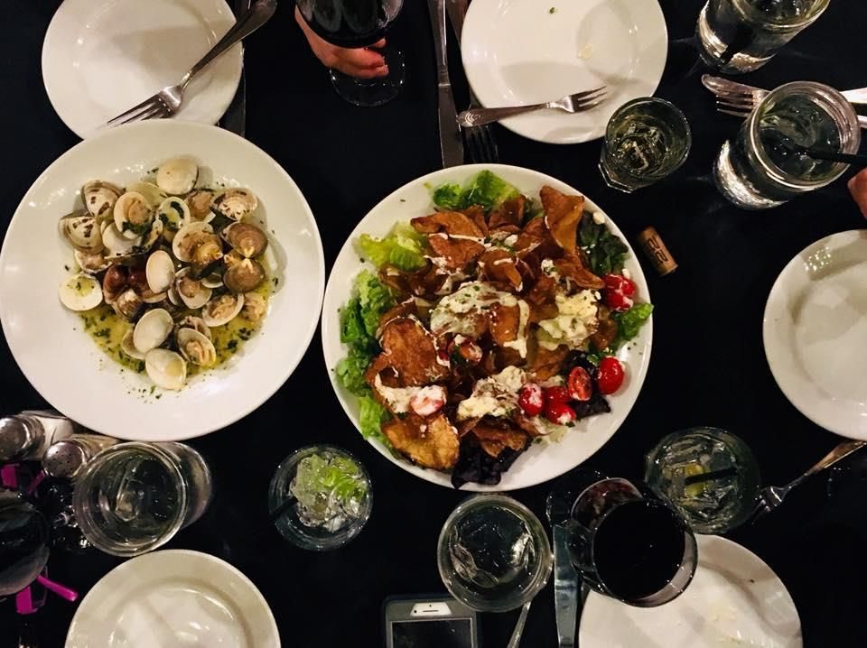 Overhead shot of a table set for a meal: two pasta dishes, glasses of wine, and white plates.