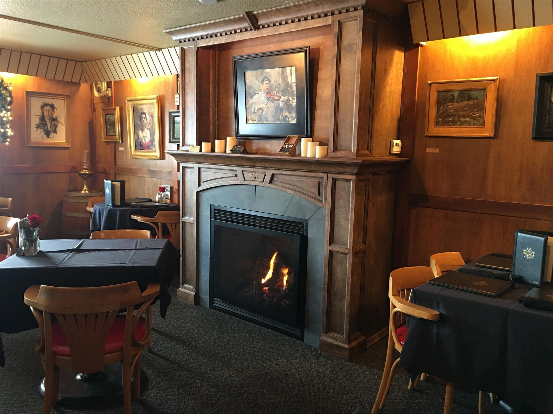 Cozy restaurant interior with a fireplace and wood paneling, tables set with black tablecloths.
