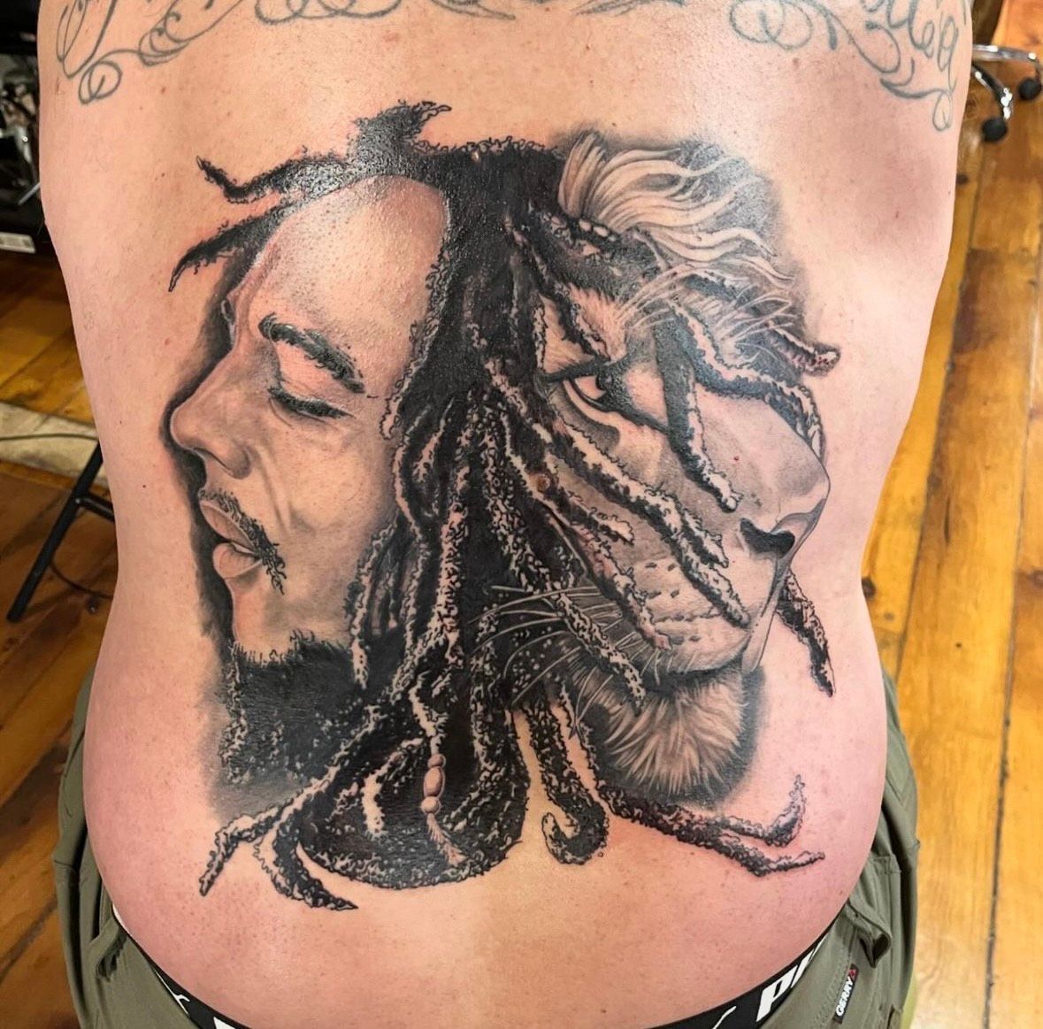 Tattoo of Bob Marley and a lion, black and grey shading on a person's back.