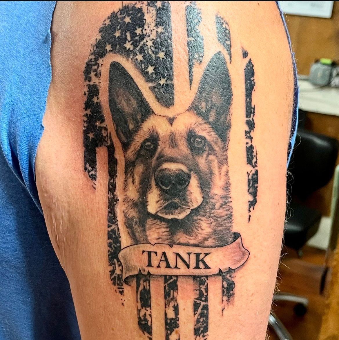 Tattoo of a German Shepherd named Tank, with an American flag background, on a person's arm.