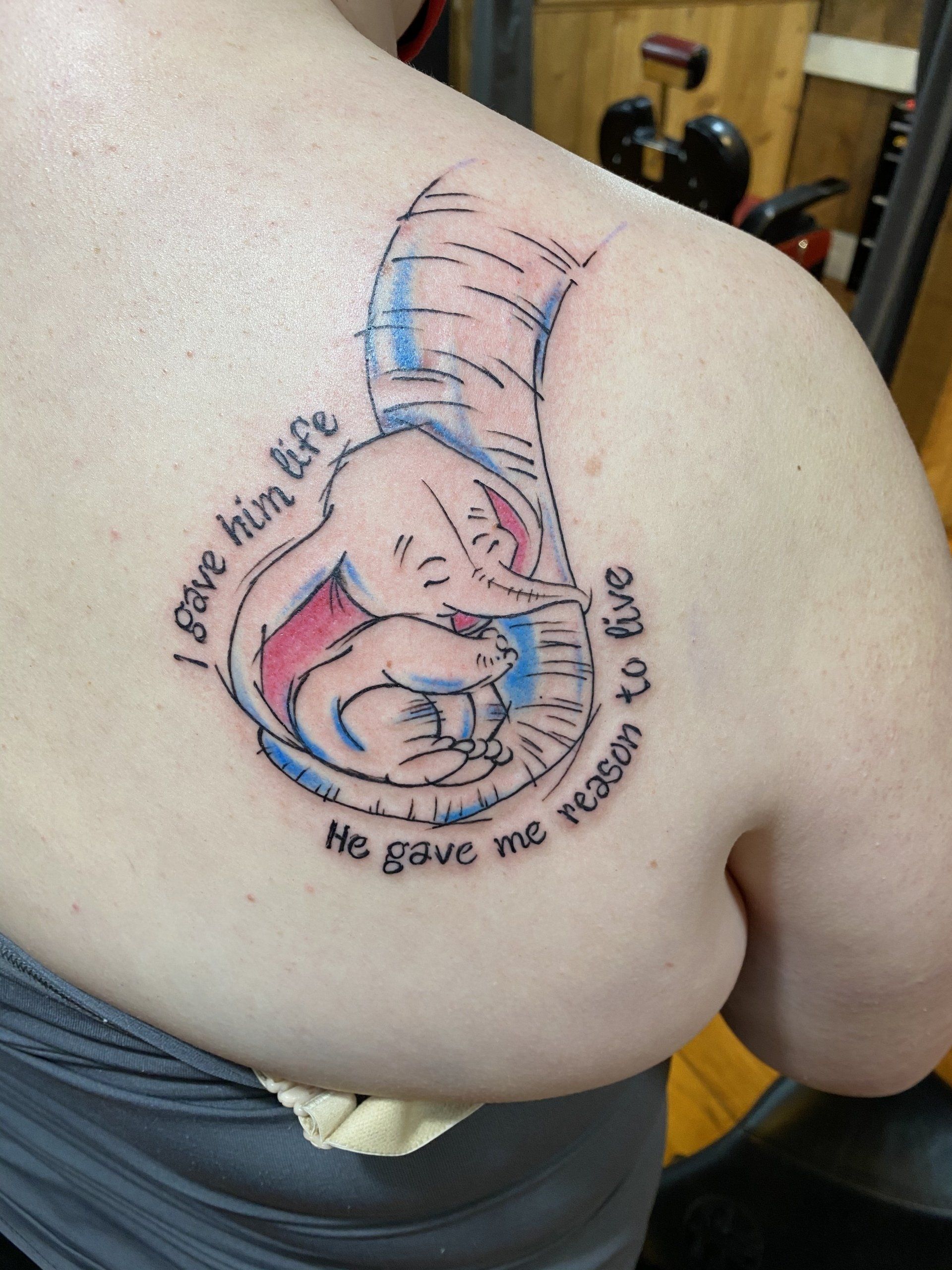 Dumbo tattoo on a shoulder: Elephant holding a baby, with quote, 