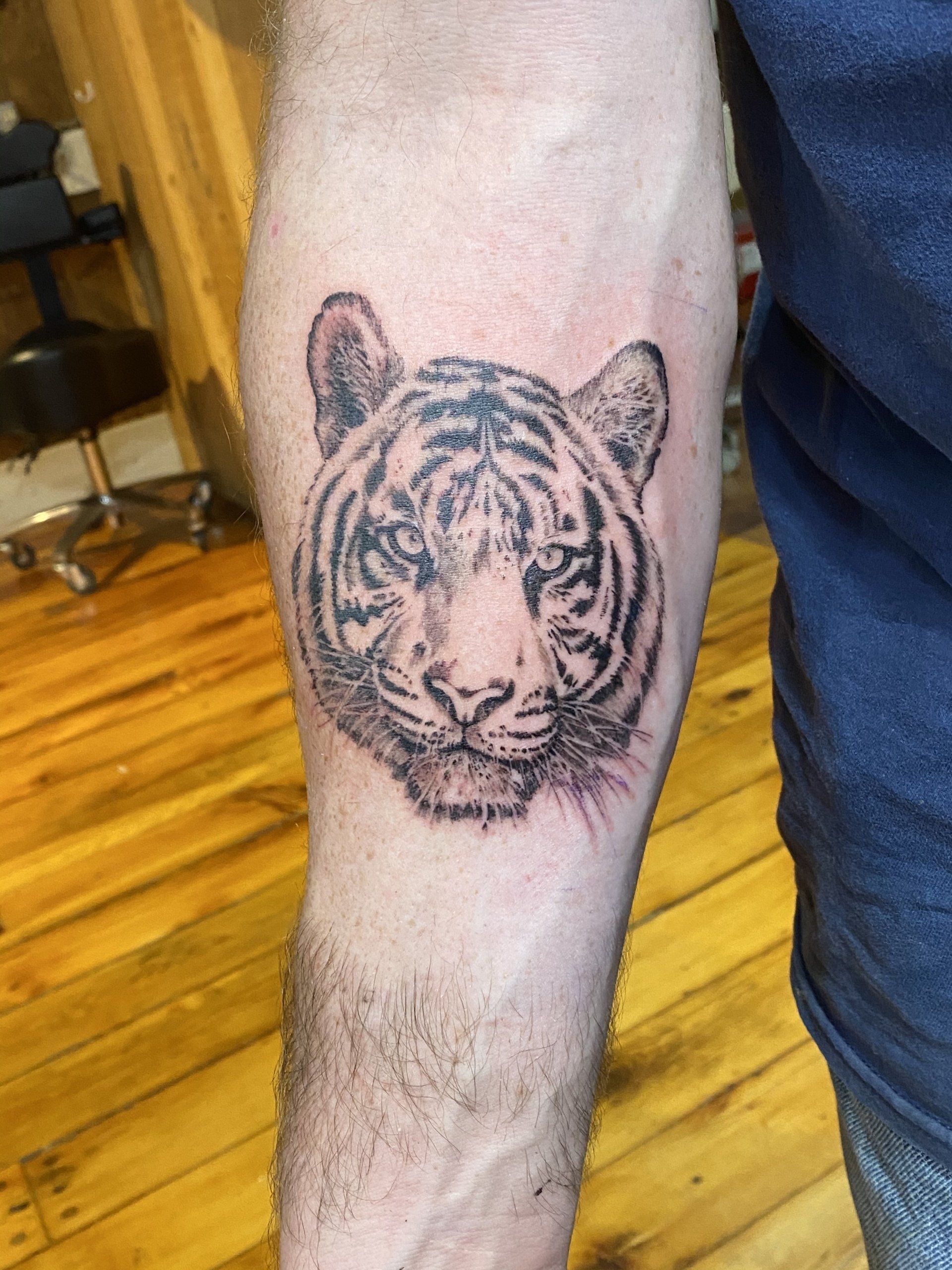 Tiger head tattoo on forearm, black ink, facing forward.