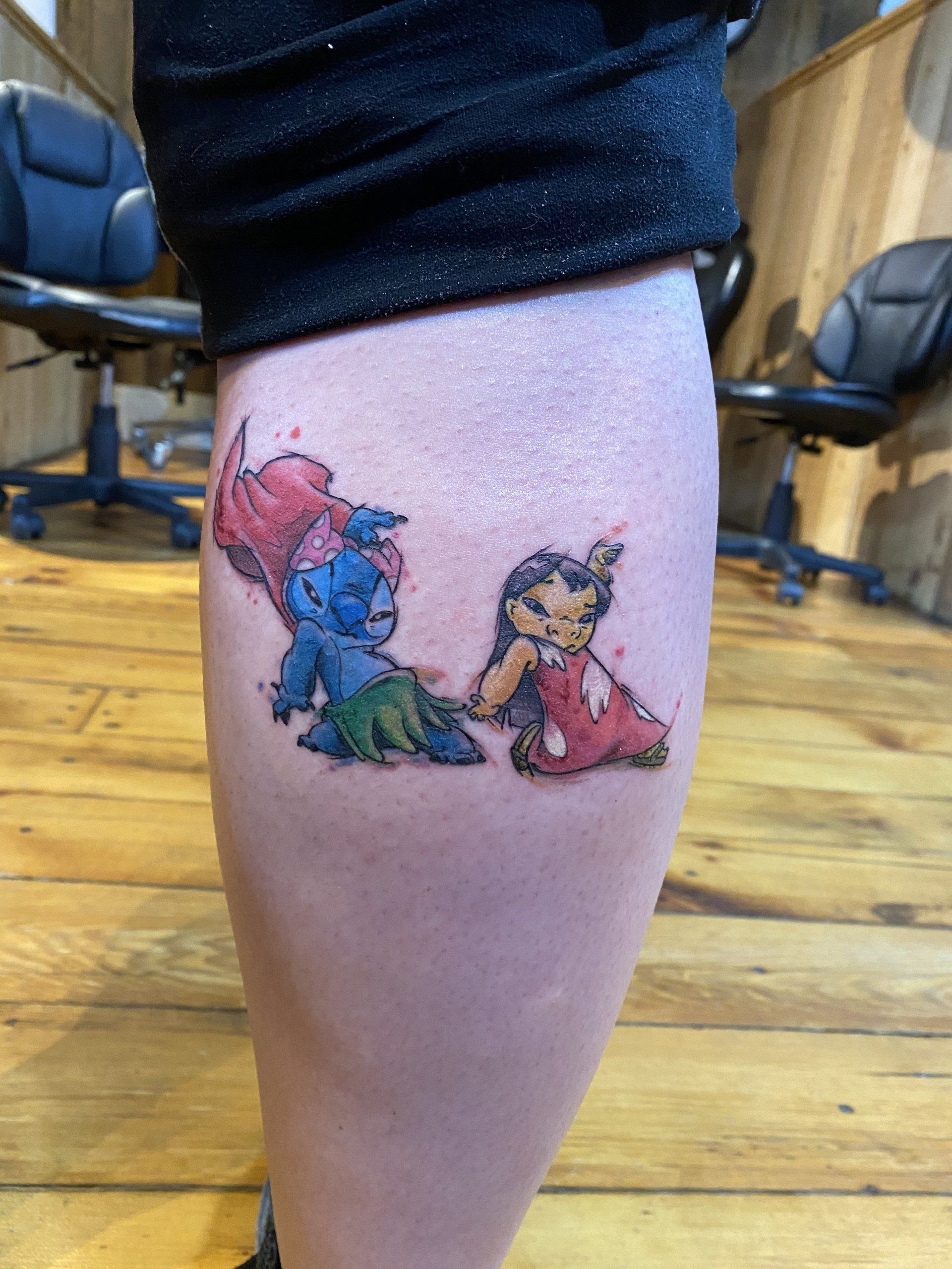 Tattoo of Lilo, Stitch, and a watercolor splash on a calf.