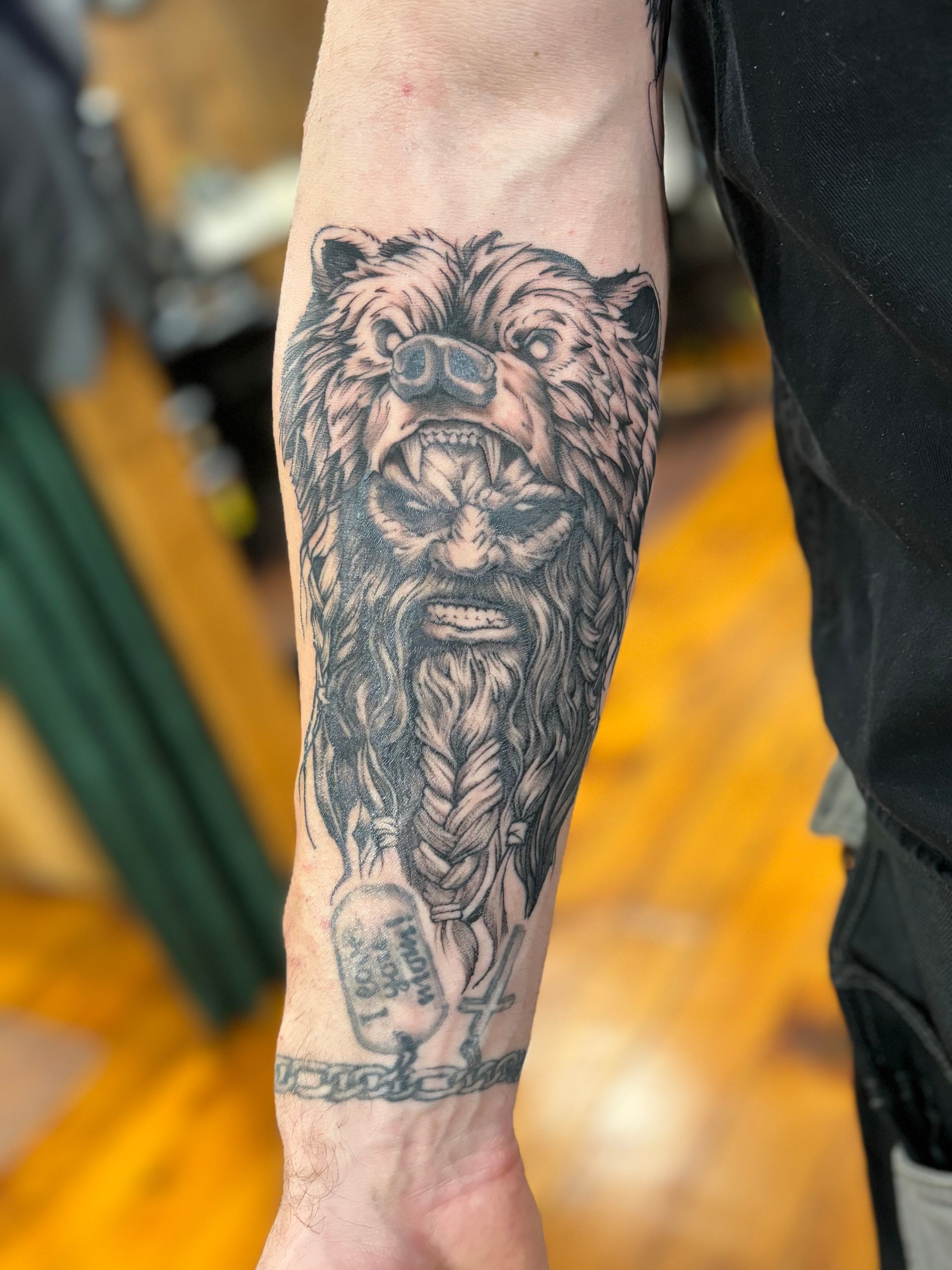 Tattoo of a bear head with a bearded face, arm. Black and gray ink.