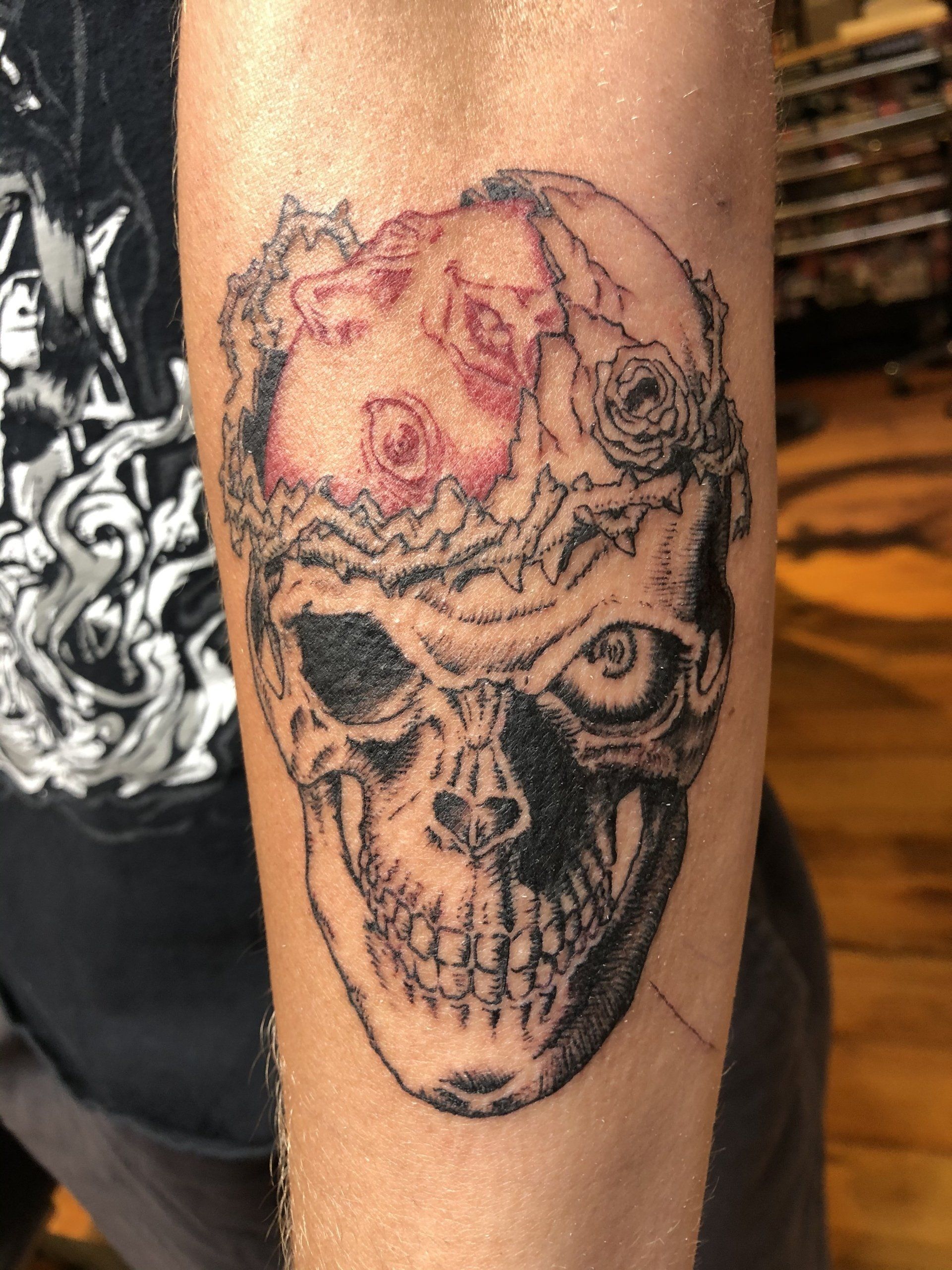 Skull tattoo with flower crown on forearm, black and white shading, with pink accents.