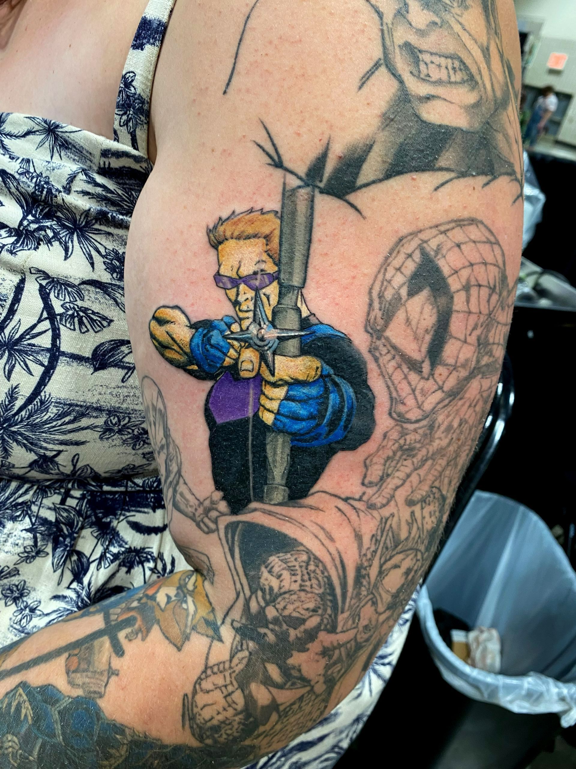 Tattoo of comic book character holding a gun. Other tattoos include Spider-Man and monsters on a person's arm.