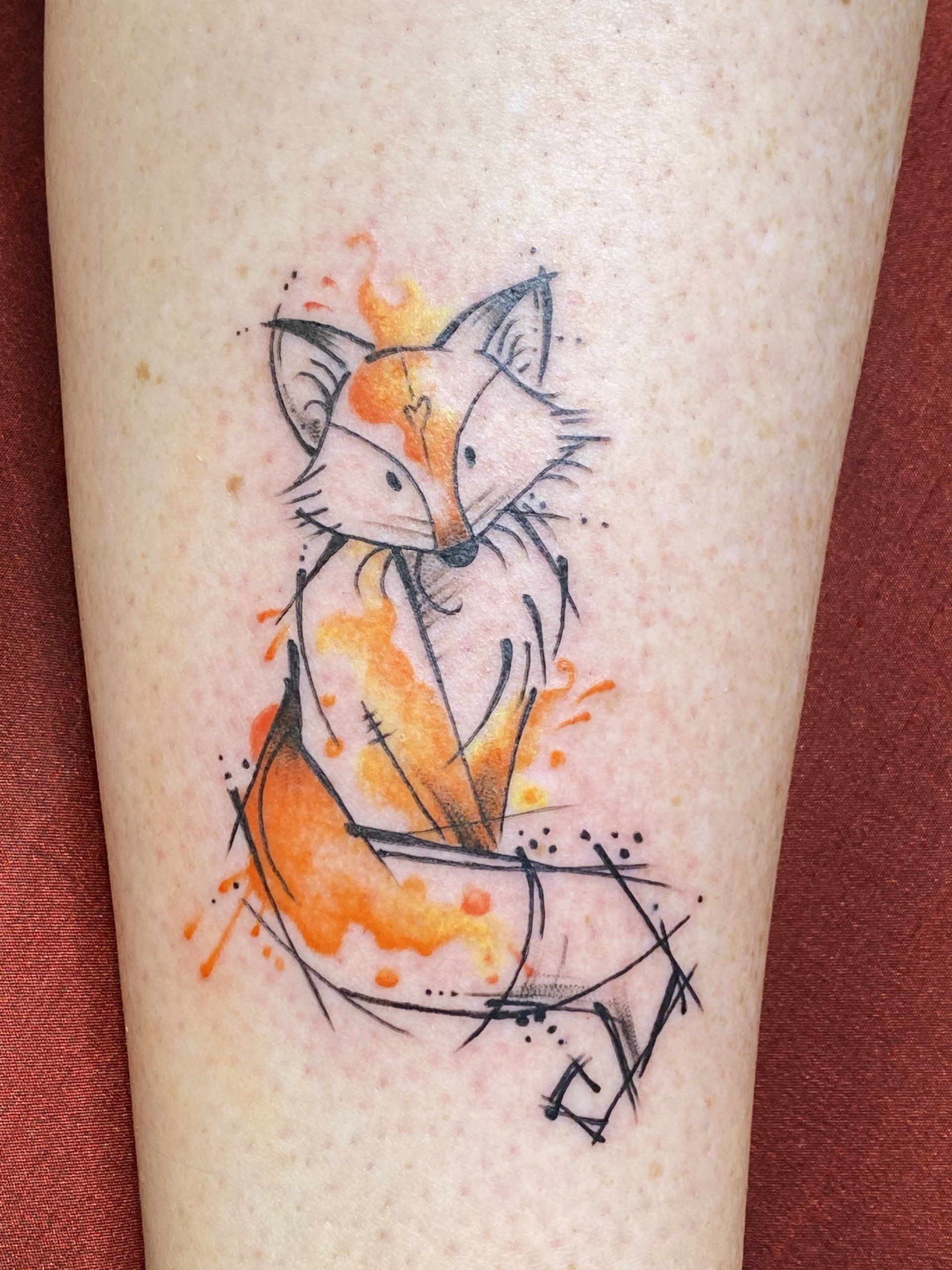 Fox tattoo with orange watercolor splashes and black linework on skin.
