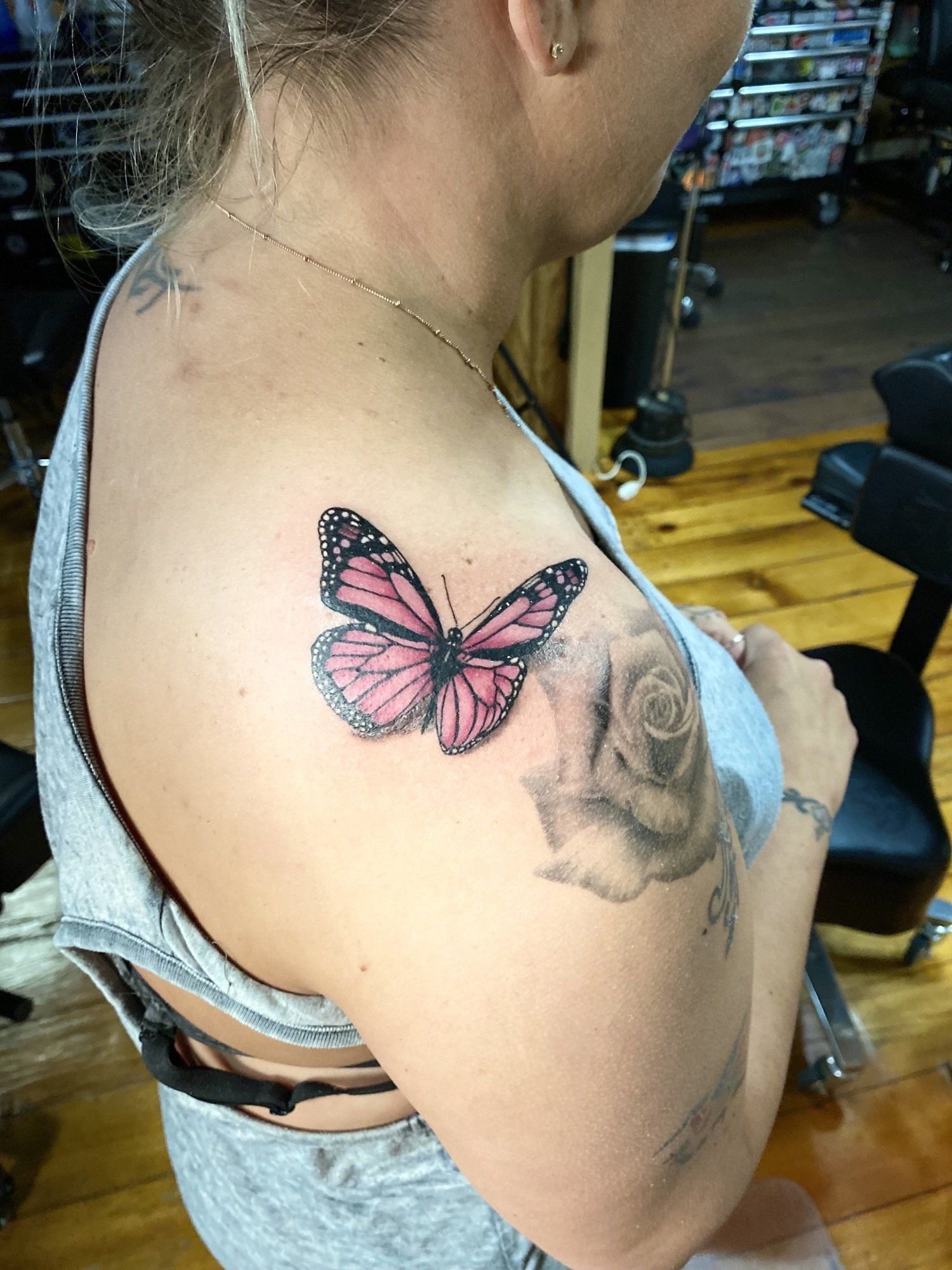 Woman's shoulder with a pink and black butterfly tattoo. A large rose tattoo is also visible.