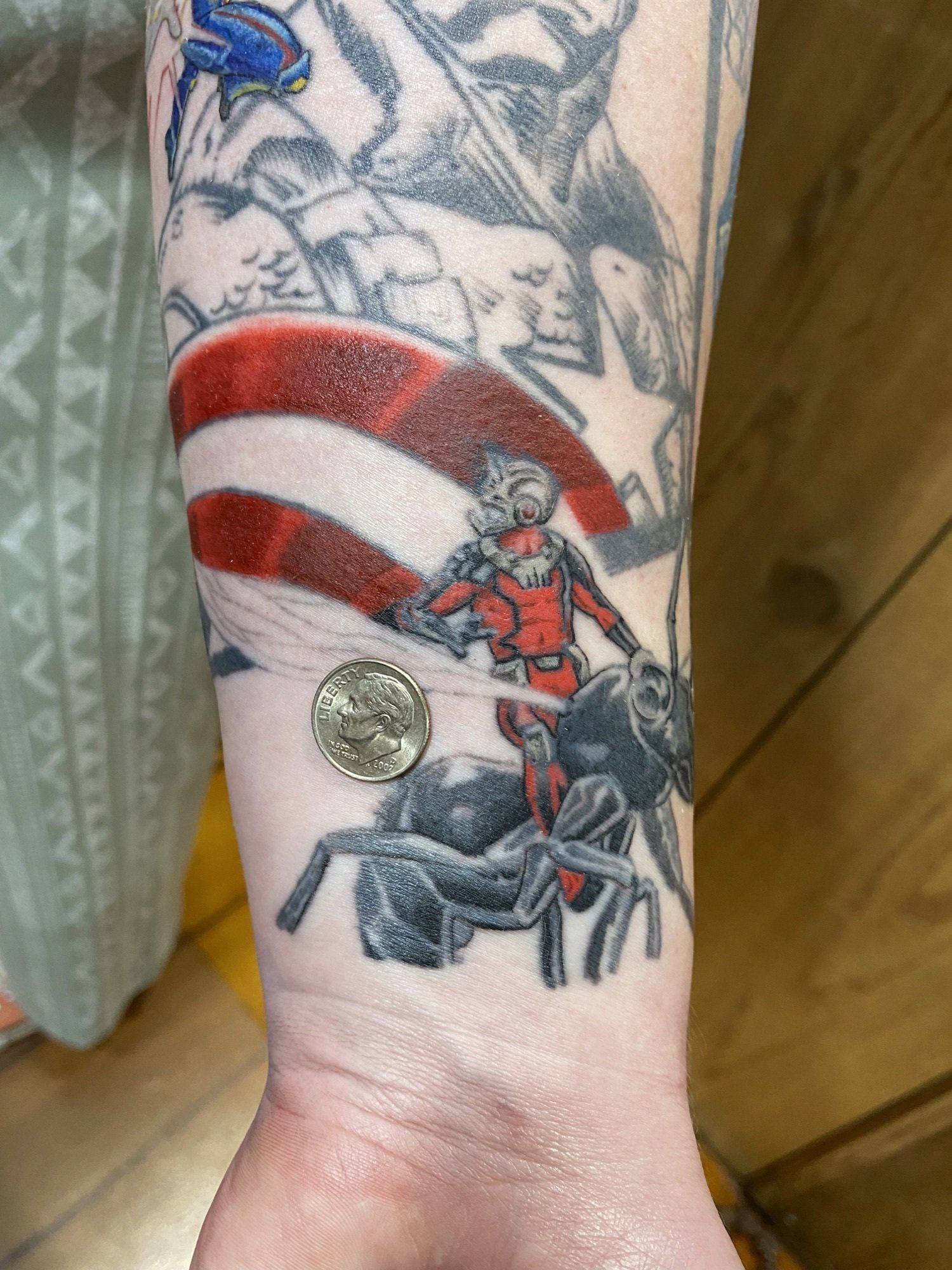 Tattoo of Ant-Man riding an ant in front of a US flag and a quarter.
