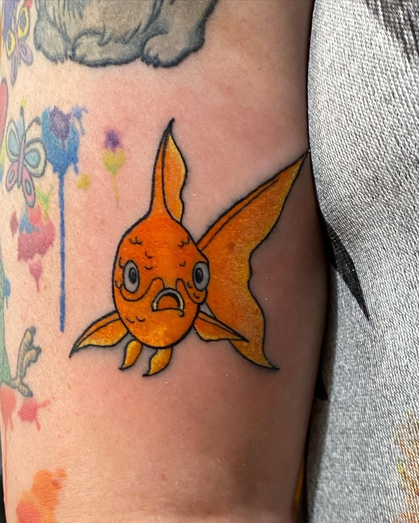 Orange goldfish tattoo on arm, with a concerned expression.