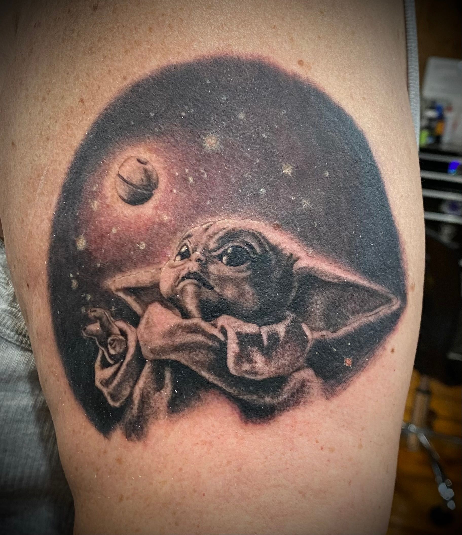 Baby Yoda tattoo, grayscale, in a starry space with a planet.