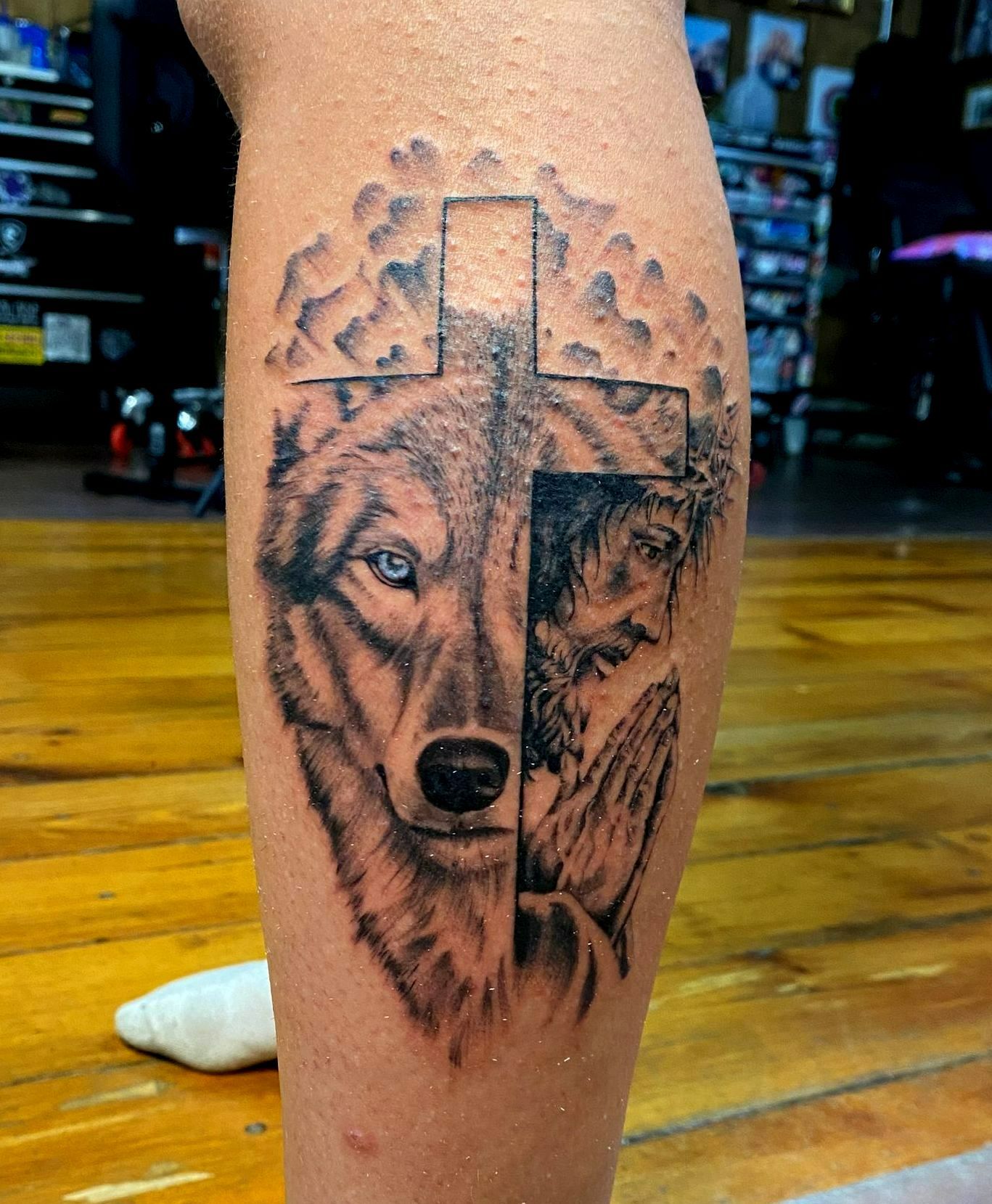 Tattoo on leg: wolf face, cross, praying hands, and clouds.