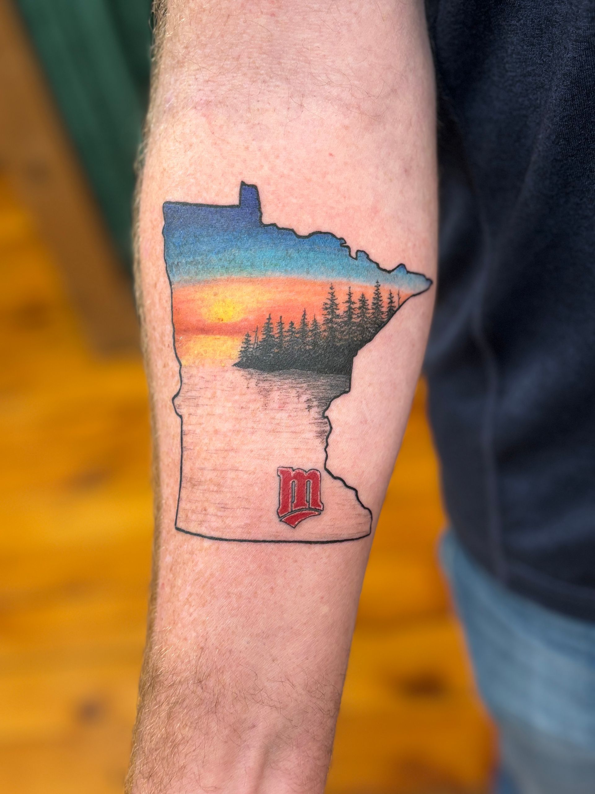 Tattoo of Minnesota outline with sunset scene and red 