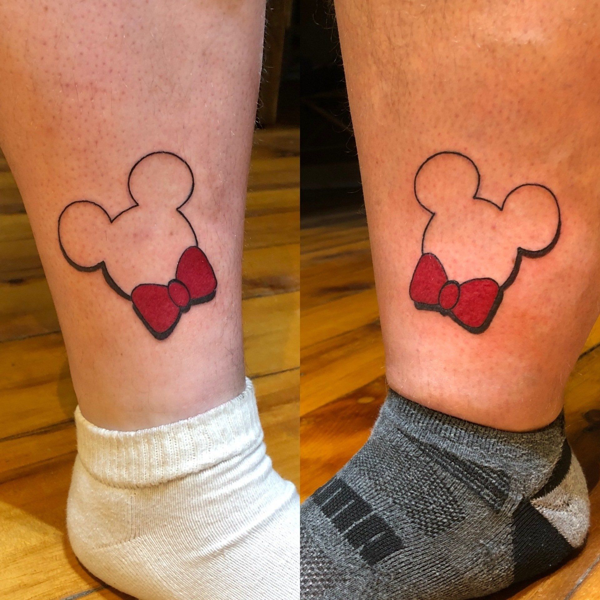 Two ankles each with a Minnie Mouse head tattoo with red bow; one leg has a white sock, the other has a gray sock.