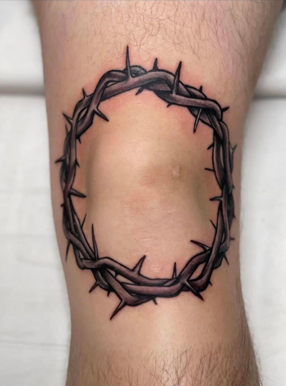 Thorned crown tattoo on a knee, in dark gray, with a light skin background.