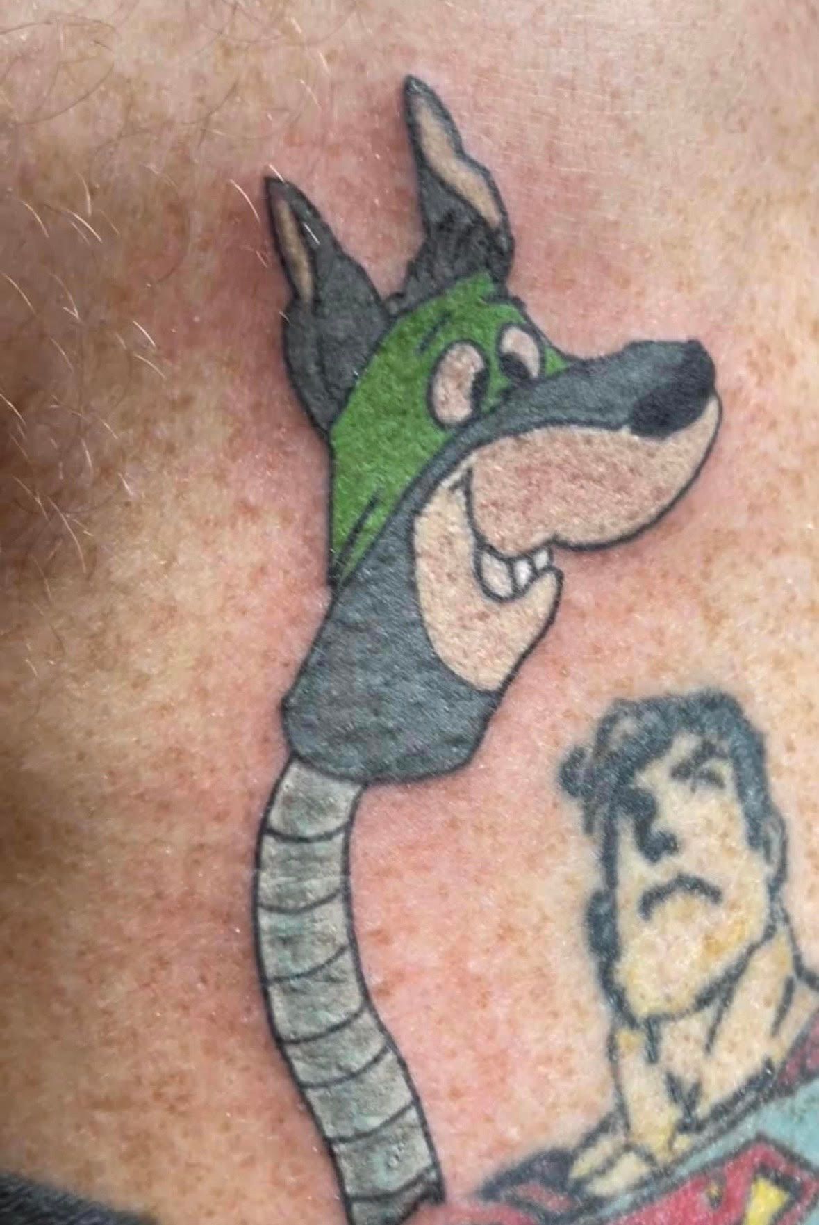 Cartoon dog with green mask, long neck, next to Superman tattoo.
