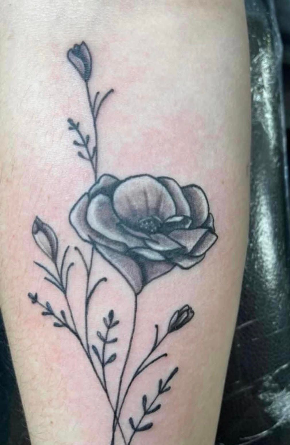 Black and gray flower tattoo on skin, featuring a large bloom, buds, and delicate stems.