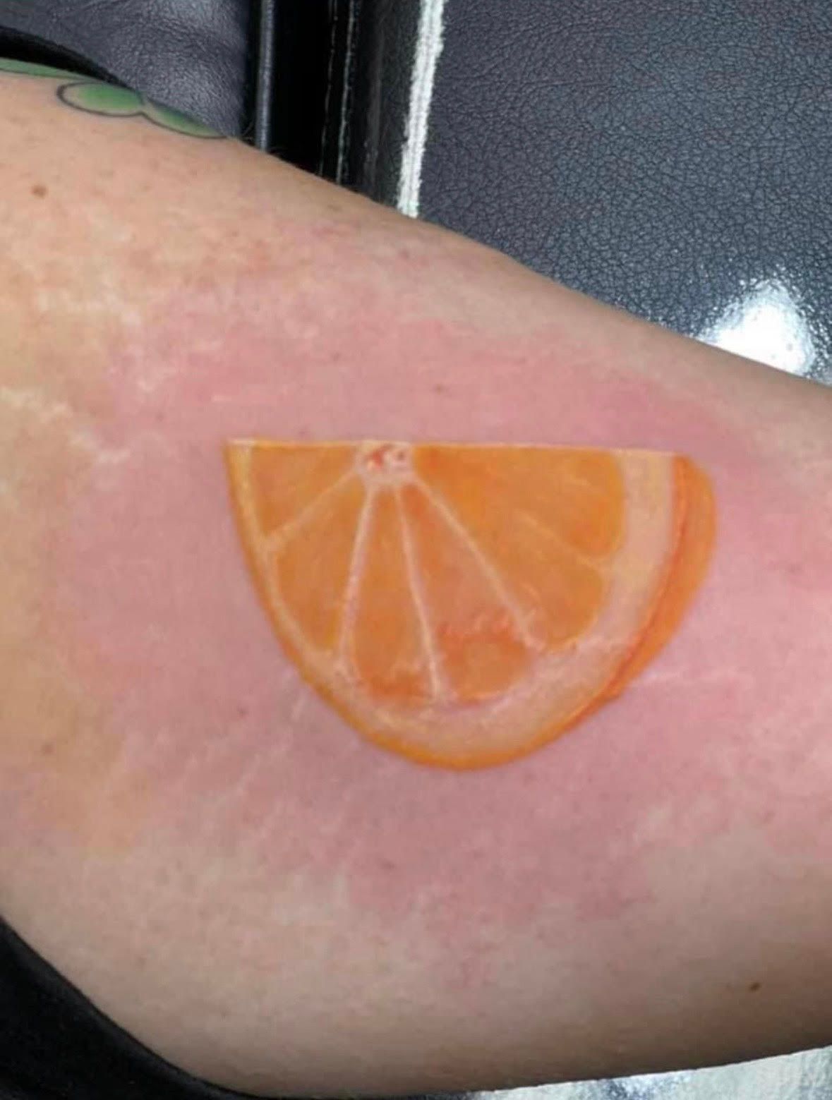 Tattoo of a tangerine slice on a person's arm, visible skin with reddish hue.
