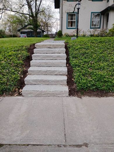 A set of light grey stone steps leading up a grassy incline toward a two-story house with a white exterior.