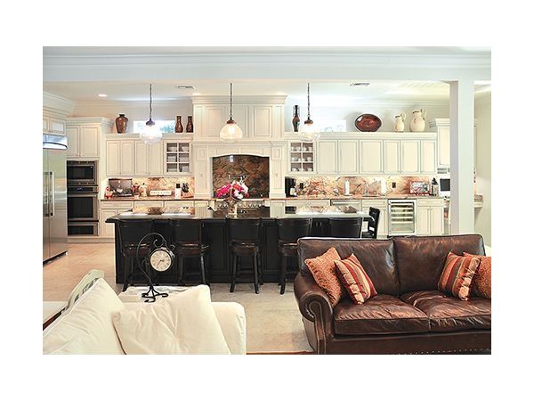 Open-concept kitchen with white cabinets, dark island, and leather sofa in living area.
