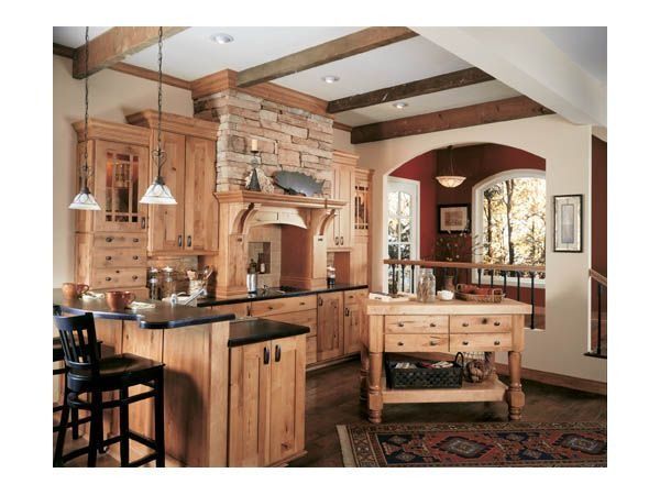 Rustic kitchen with wood cabinets, stone range hood, island, and arched doorway.