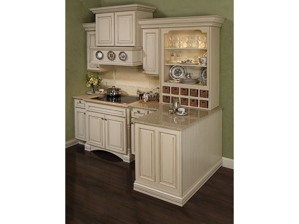 Cream-colored kitchen cabinets with granite countertop, built-in stove and display case against a green wall and dark wood floor.