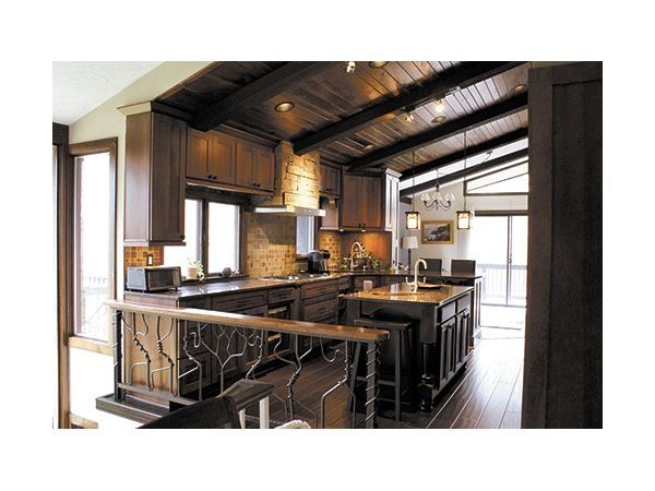 Dark wood kitchen with cabinetry, island, and angled ceiling. Includes a stone backsplash and a decorative railing.