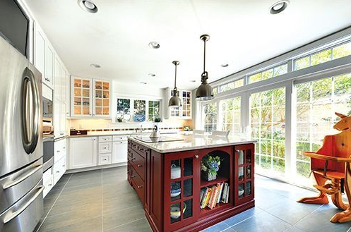 Oval bathtub in a bathroom, next to two windows with blinds. Gold faucet, white cabinetry and wall, beige walls.