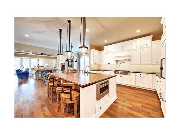 Spacious white kitchen with wood floor, large island, pendant lights, and stainless steel appliances.