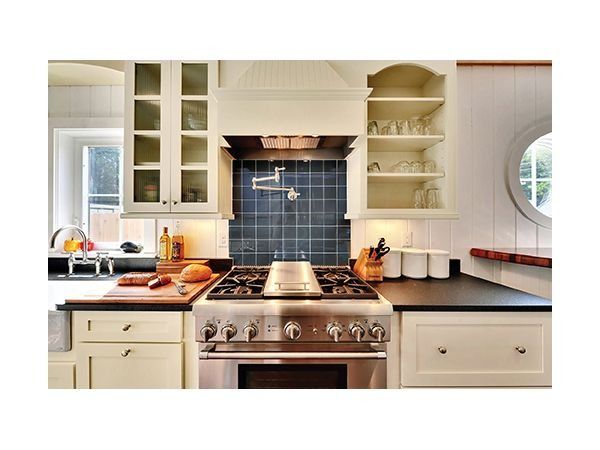 Kitchen with stainless steel range, dark blue tile backsplash, light cabinets, and a round window.