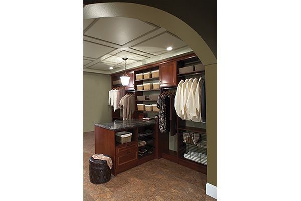 Walk-in closet with dark wood shelving, hanging clothes, baskets, and a central island.