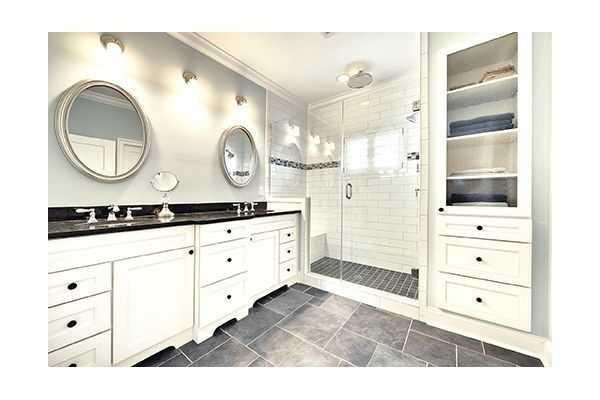 Modern bathroom with white vanity, shower, and built-in storage. Blue walls, stone floor.