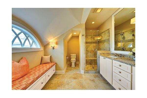 Bathroom with arched window and built-in bench. Beige walls, stone floor, shower, and vanity.